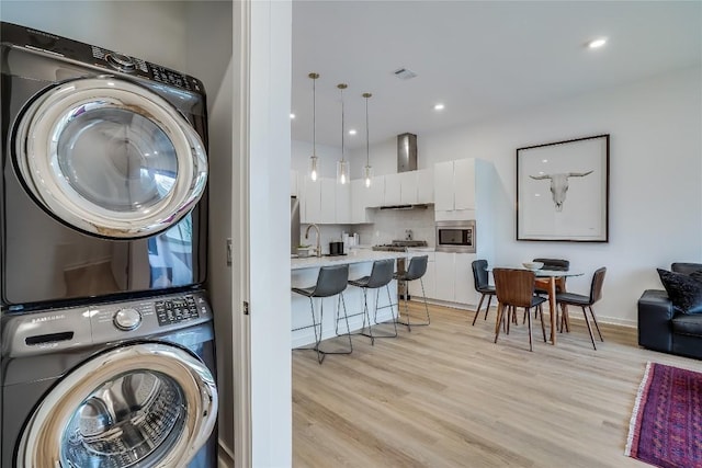 clothes washing area featuring laundry area, light wood-style flooring, recessed lighting, and stacked washing maching and dryer