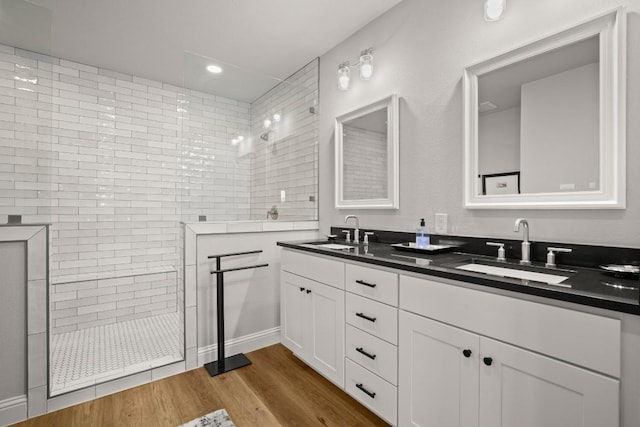 bathroom with double vanity, wood finished floors, a walk in shower, and a sink