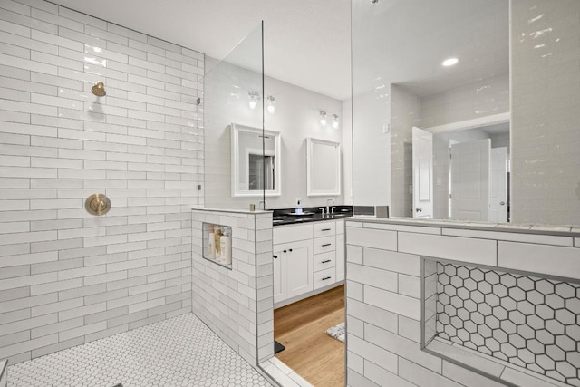 full bath with tiled shower, vanity, and wood finished floors