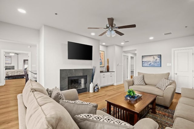 living area with a tiled fireplace, recessed lighting, light wood-style floors, and visible vents