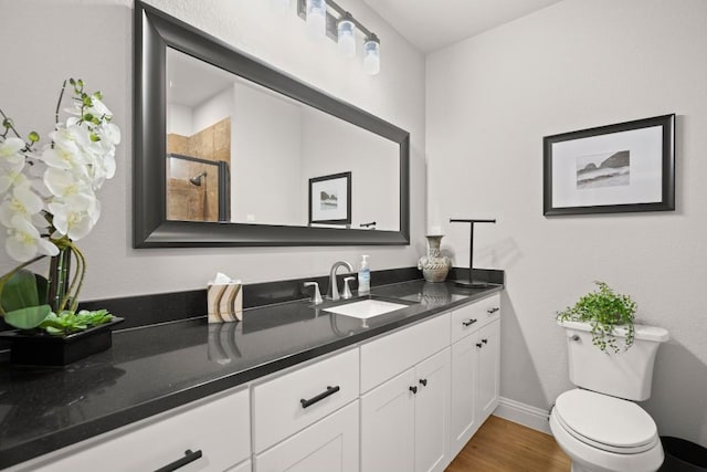 bathroom with toilet, a stall shower, wood finished floors, baseboards, and vanity