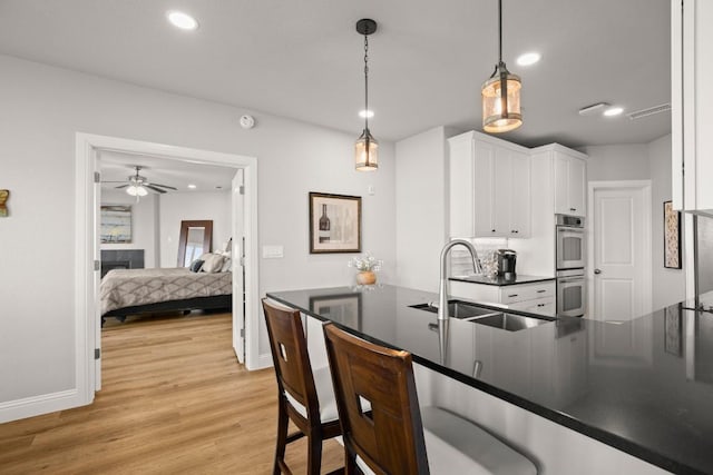 kitchen with dark countertops, a sink, white cabinets, double oven, and decorative light fixtures