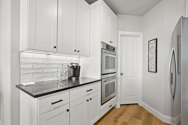 kitchen featuring dark countertops, white cabinetry, light wood-style floors, appliances with stainless steel finishes, and decorative backsplash