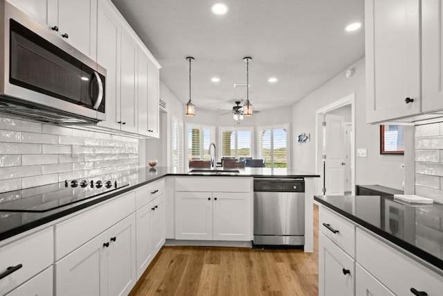 kitchen with a sink, dark countertops, stainless steel appliances, a peninsula, and light wood finished floors