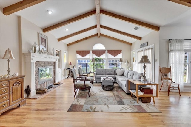 living area with a glass covered fireplace, beamed ceiling, visible vents, and wood finished floors