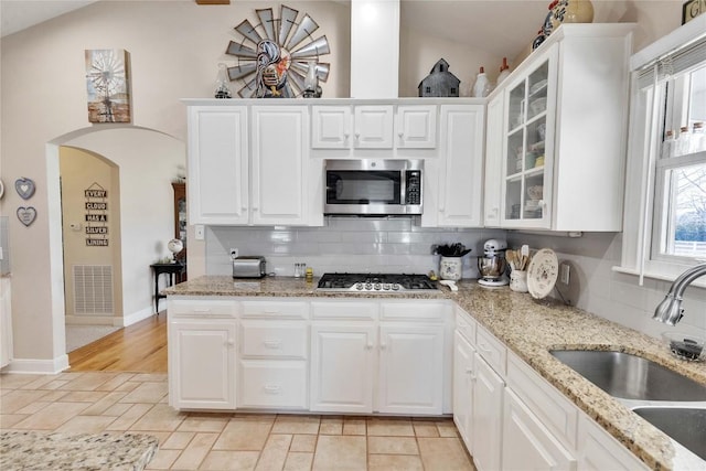 kitchen featuring arched walkways, appliances with stainless steel finishes, lofted ceiling, and a sink