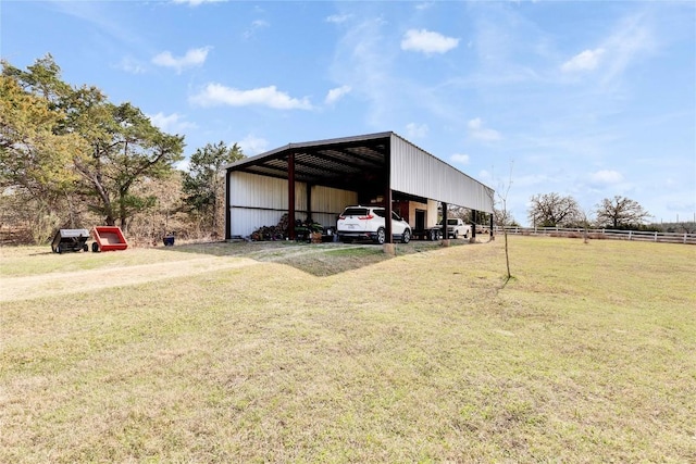 view of pole building with a lawn, a detached carport, dirt driveway, and fence