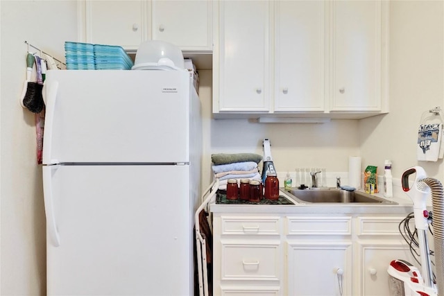 kitchen with white cabinets, light countertops, freestanding refrigerator, and a sink