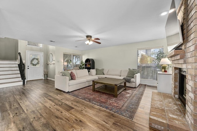 living area with visible vents, a brick fireplace, stairway, a ceiling fan, and wood-type flooring