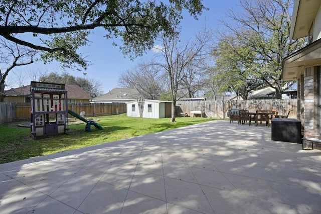 view of patio featuring outdoor dining space, an outbuilding, a shed, a fenced backyard, and a playground