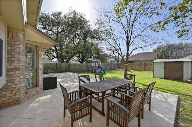 view of patio / terrace with an outbuilding, a shed, outdoor dining area, a fenced backyard, and a playground