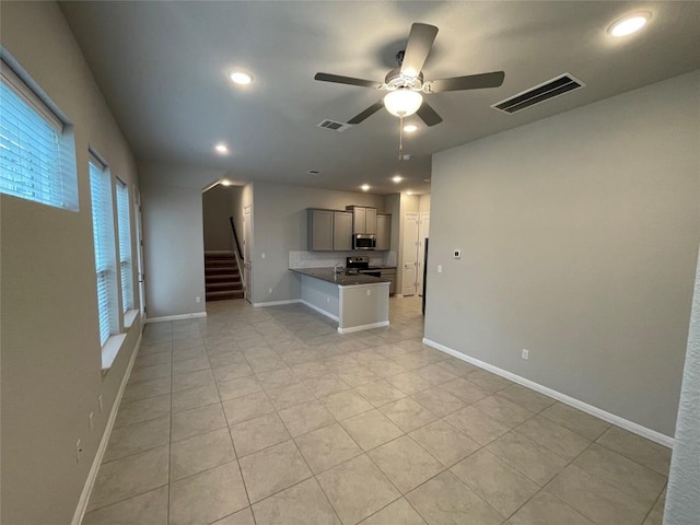 unfurnished living room with visible vents, baseboards, a ceiling fan, and stairs