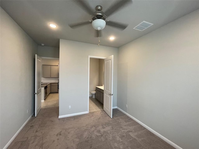 unfurnished bedroom with visible vents, light colored carpet, connected bathroom, and baseboards