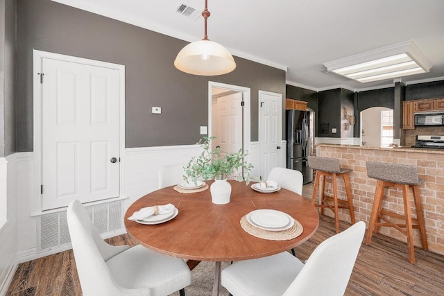 dining area featuring a wainscoted wall, arched walkways, visible vents, and wood finished floors