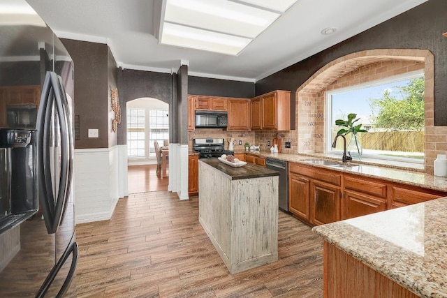 kitchen featuring light wood-type flooring, stainless steel appliances, wainscoting, and a sink