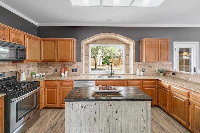 kitchen with a sink, a kitchen island, backsplash, appliances with stainless steel finishes, and light wood finished floors