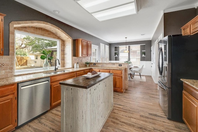 kitchen featuring a wealth of natural light, appliances with stainless steel finishes, a peninsula, wood finished floors, and a sink