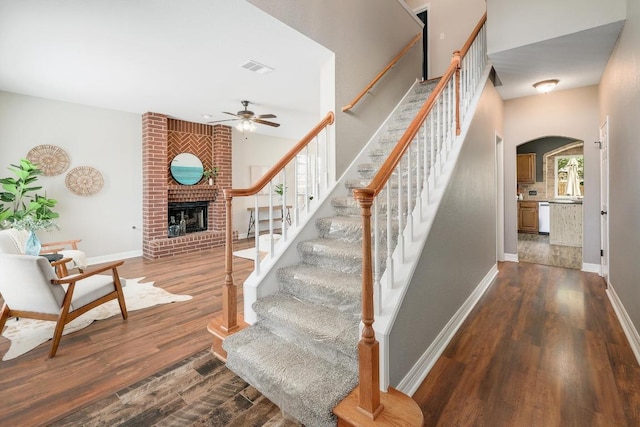 stairway with wood finished floors, baseboards, visible vents, a fireplace, and arched walkways