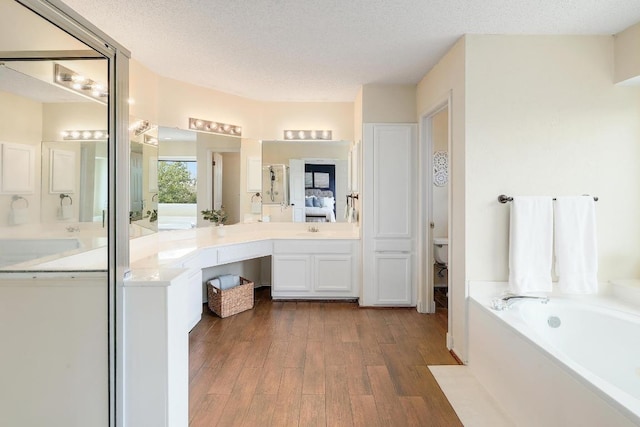 full bathroom featuring vanity, a bath, wood finished floors, a textured ceiling, and toilet