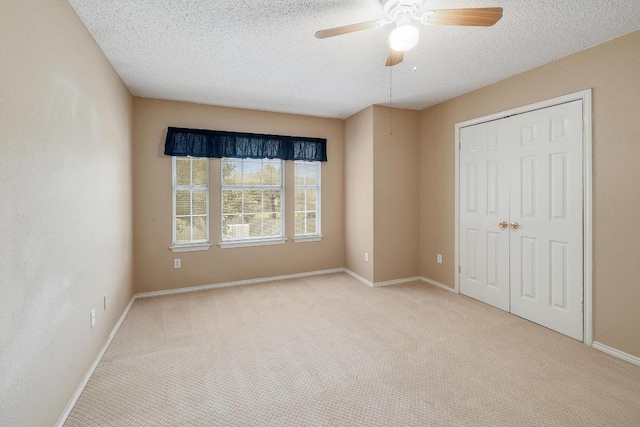 unfurnished bedroom featuring baseboards, carpet, a closet, a textured ceiling, and a ceiling fan