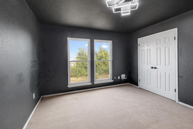 unfurnished bedroom featuring carpet, baseboards, a textured wall, and a textured ceiling