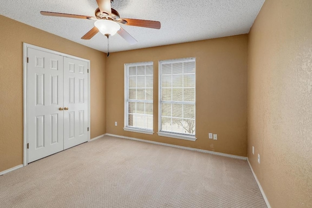 unfurnished bedroom featuring a ceiling fan, a textured ceiling, a closet, carpet floors, and a textured wall