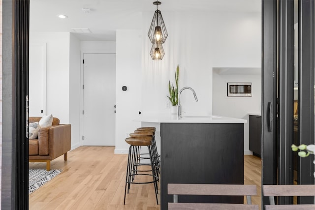 kitchen with decorative light fixtures, a breakfast bar area, light countertops, light wood-style floors, and a sink