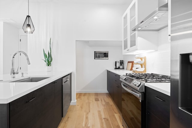 kitchen with light countertops, appliances with stainless steel finishes, modern cabinets, wall chimney exhaust hood, and a sink