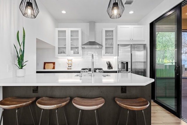 kitchen with a kitchen bar, tasteful backsplash, wall chimney exhaust hood, stainless steel fridge with ice dispenser, and light countertops