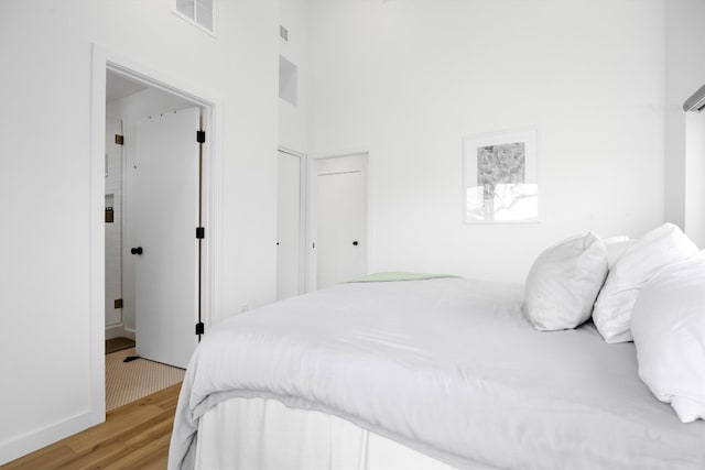 bedroom featuring visible vents, a high ceiling, and light wood-style flooring