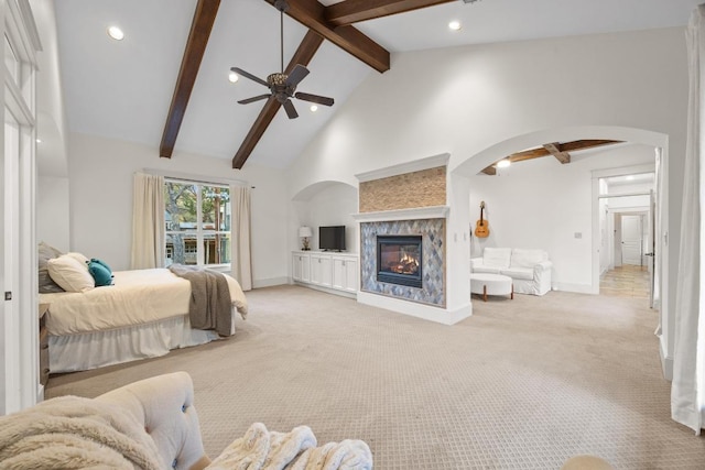 bedroom with high vaulted ceiling, beam ceiling, arched walkways, light carpet, and a glass covered fireplace