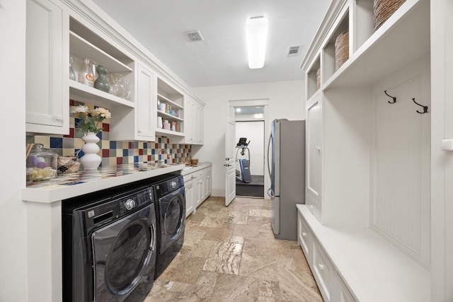 clothes washing area with washer and dryer, cabinet space, visible vents, and stone tile flooring