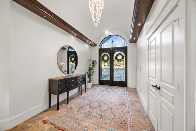 foyer entrance with lofted ceiling, stone finish flooring, french doors, an inviting chandelier, and baseboards