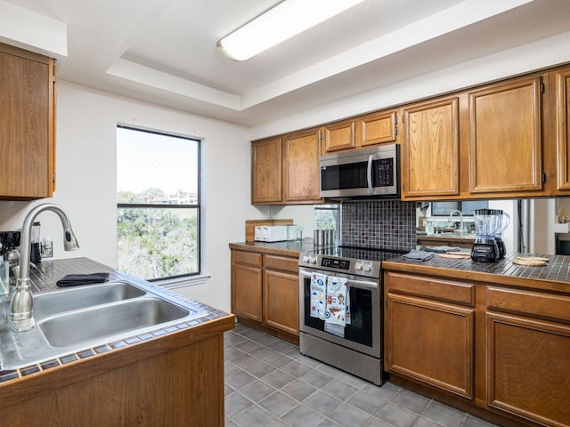 8200 Neely Dr Unit 251, Austin, TX 78759 - kitchen with stainless steel appliances, a sink, brown cabinetry, a tray ceiling, and tile countertops