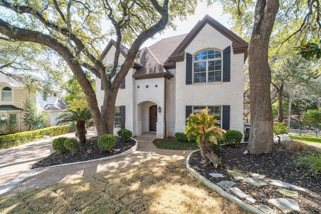 french country inspired facade with a shingled roof and stucco siding