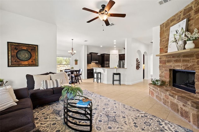 living area with visible vents, light tile patterned flooring, a fireplace, arched walkways, and ceiling fan with notable chandelier