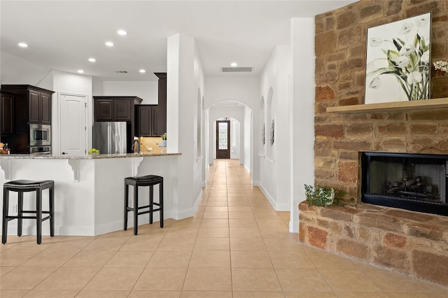 kitchen with stainless steel appliances, arched walkways, a breakfast bar area, light tile patterned floors, and light stone countertops