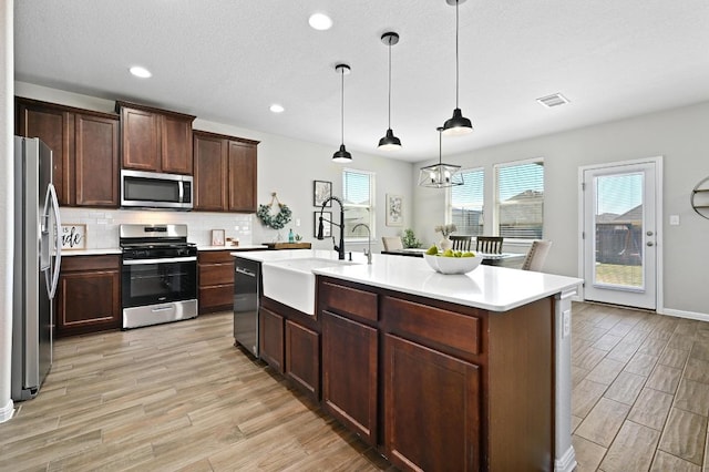 kitchen with a sink, decorative backsplash, appliances with stainless steel finishes, and light wood finished floors