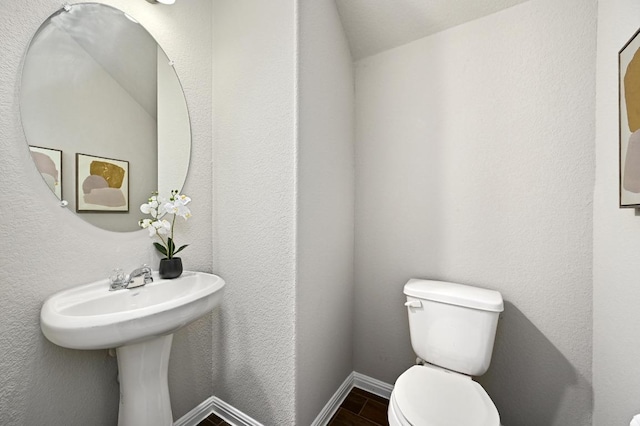 half bath featuring wood finished floors, toilet, a textured wall, and baseboards