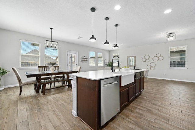 kitchen featuring decorative light fixtures, light wood-type flooring, light countertops, stainless steel dishwasher, and a sink