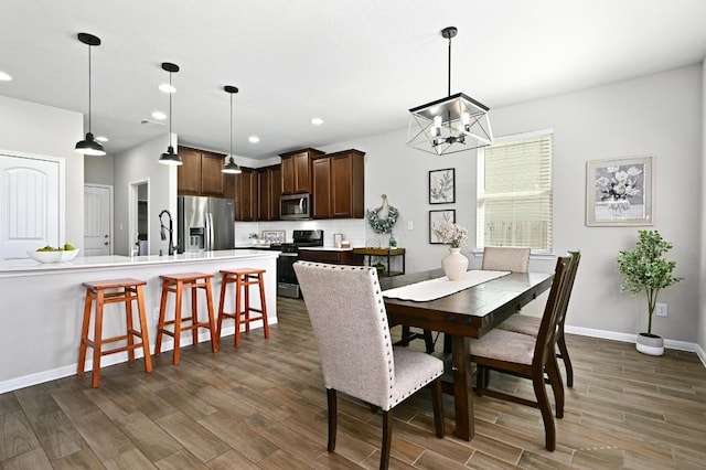 dining space with dark wood-type flooring, a notable chandelier, recessed lighting, and baseboards