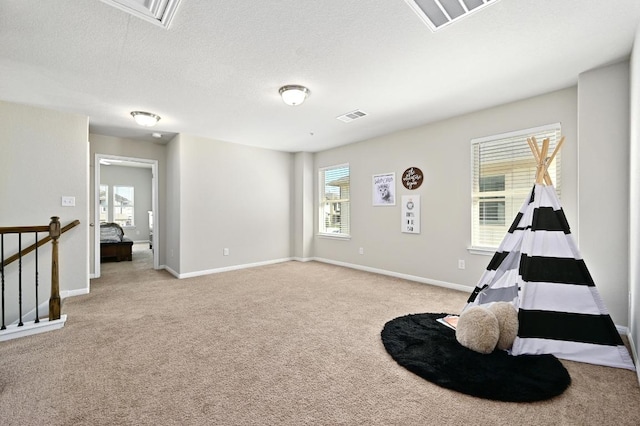 playroom with visible vents, light carpet, a textured ceiling, and attic access