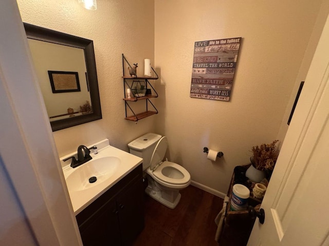 half bathroom with toilet, vanity, baseboards, and wood finished floors