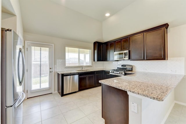 kitchen with light stone countertops, a peninsula, decorative backsplash, vaulted ceiling, and appliances with stainless steel finishes