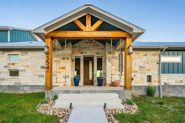 view of exterior entry with stone siding, covered porch, and board and batten siding