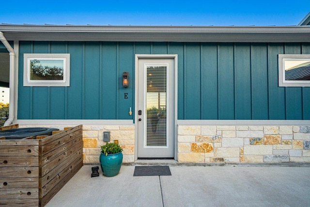 entrance to property featuring a patio area, stone siding, and board and batten siding