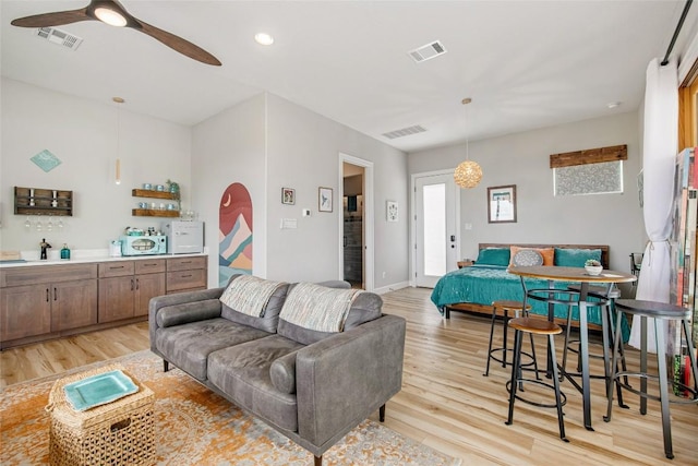 living room with visible vents, light wood finished floors, and ceiling fan