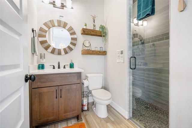 bathroom with a shower stall, baseboards, toilet, wood finished floors, and vanity