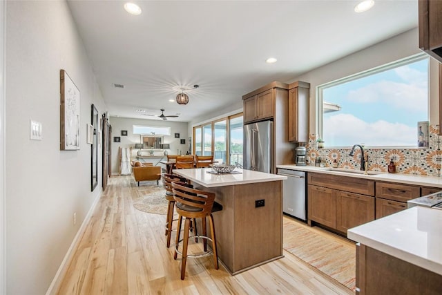 kitchen featuring a center island, light wood-type flooring, decorative backsplash, appliances with stainless steel finishes, and a sink