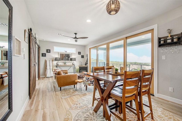 dining space featuring a barn door, light wood-style flooring, baseboards, and visible vents